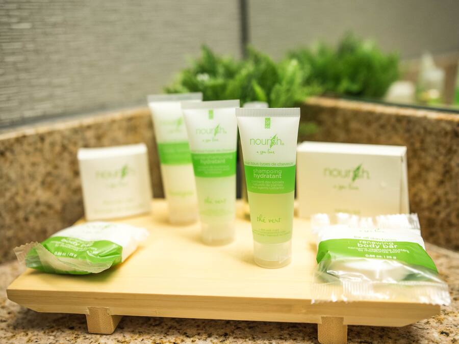 A wooden tray with various Nourish brand skincare products, including a body bar and a hydrating shampoo, on a granite countertop.