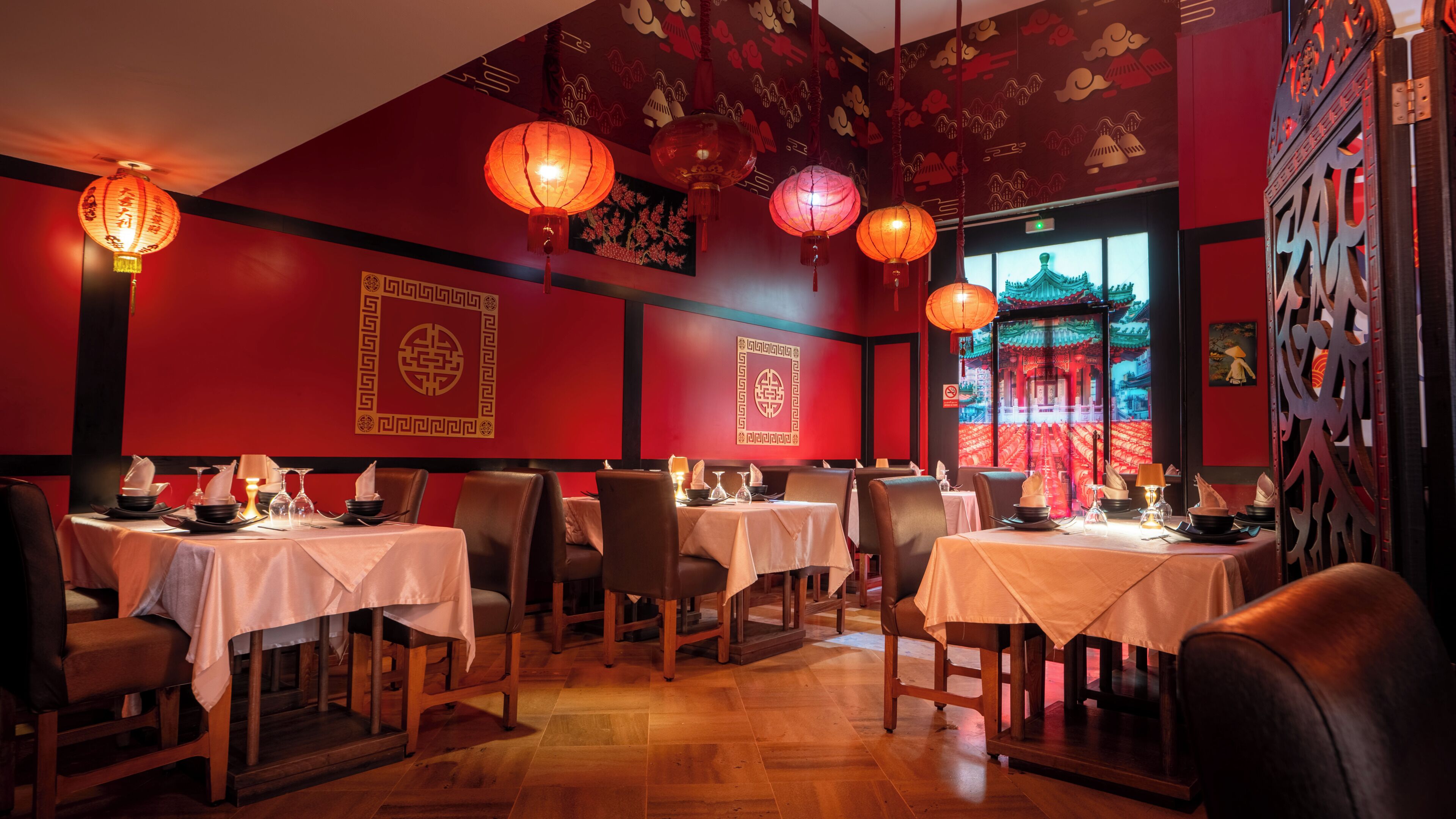 A restaurant with tables set for dining, traditional lanterns, and red walls with Chinese characters.