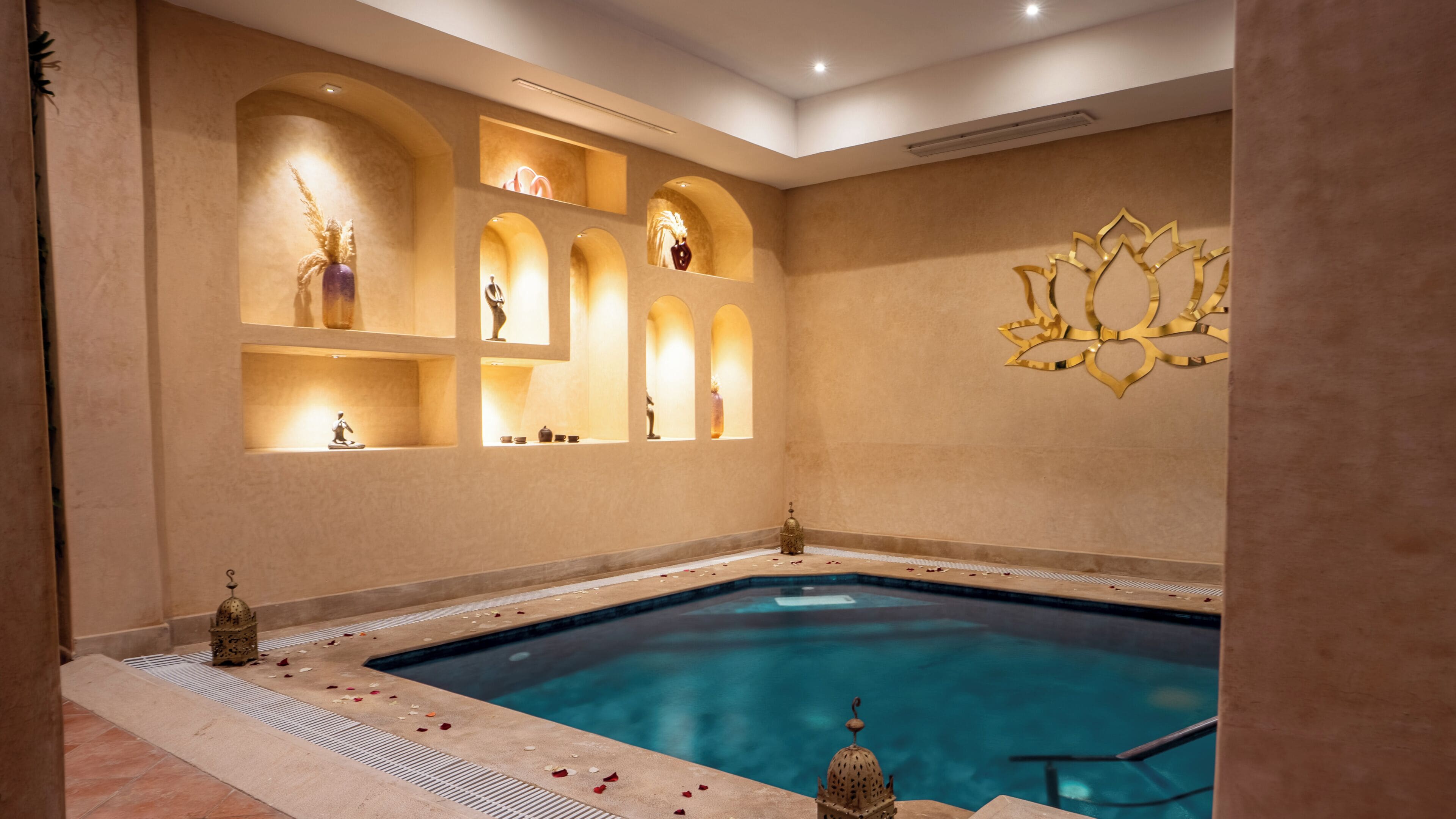 A spa area with a pool, arched alcoves with decorative items, and a wall-mounted golden ornament.