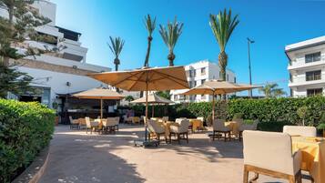 Un patio exterior con mesas, sillas, sombrillas y palmeras.