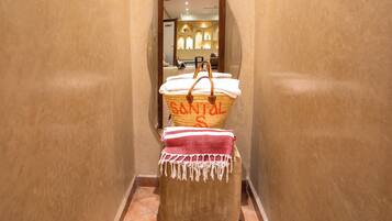 A hallway with a woven basket on a stool, a red and white patterned cloth, and a glimpse of a room with a mirror and lights.