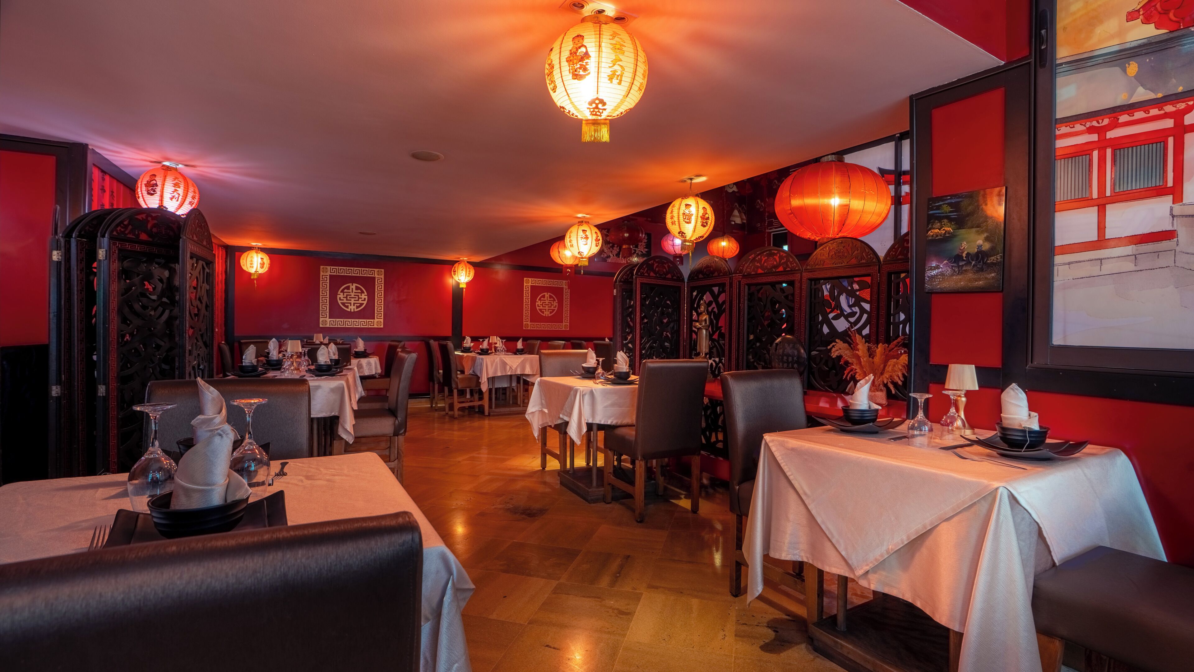 Un interior de restaurante con mesas dispuestas para comer, decoración tradicional y faroles colgantes.
