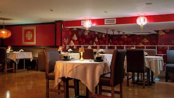 Interior de un restaurante con mesas preparadas para comer, paredes con diseño rojo y faroles colgantes.