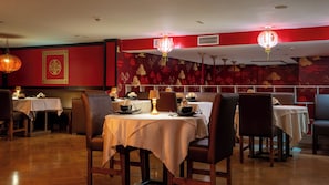 Ein Restaurantinneres mit gedeckten Tischen, roten Wänden mit Muster und hängenden Laternen.