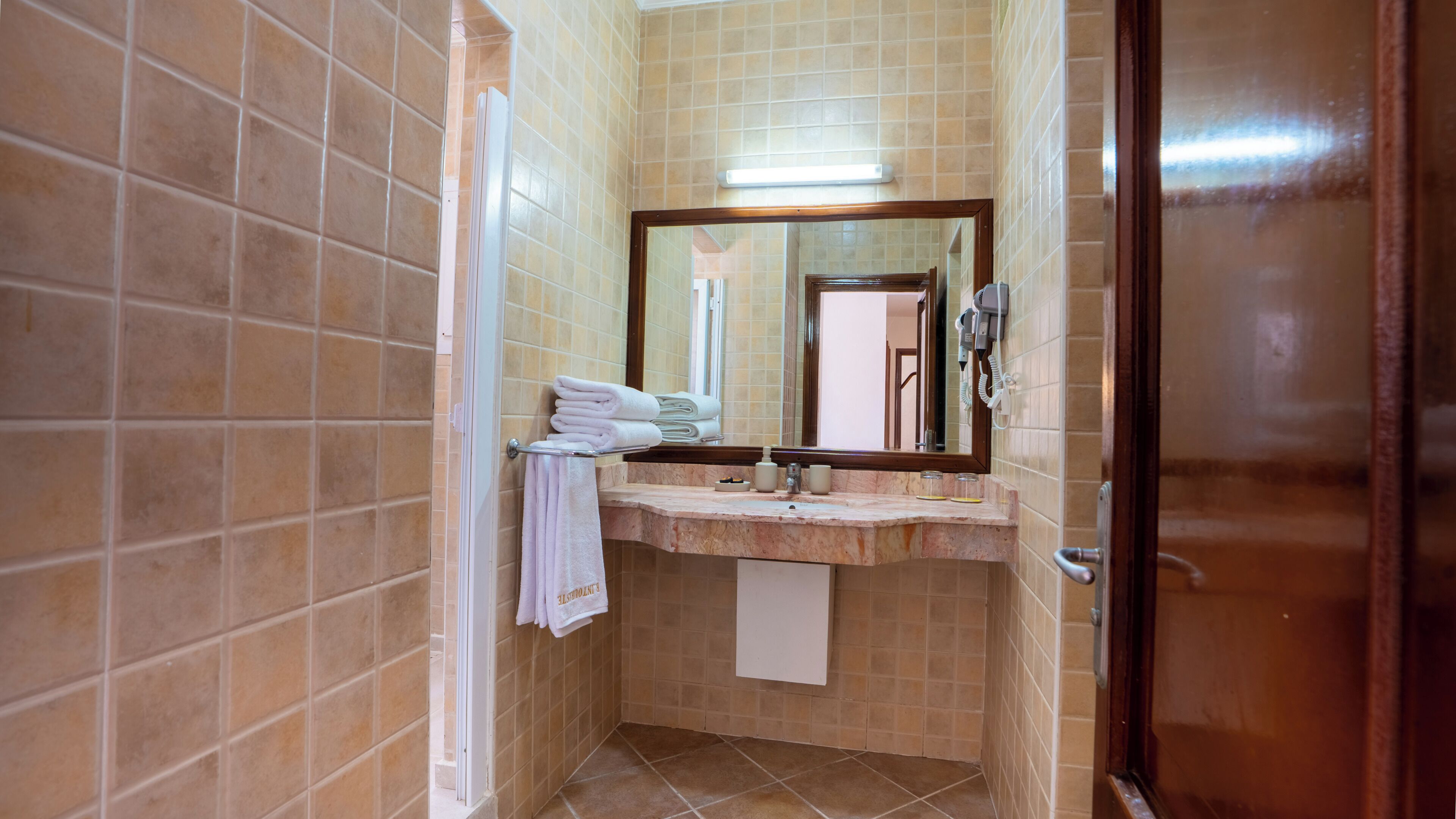 A bathroom with a tiled wall, a sink with a mirror, and a towel rack.