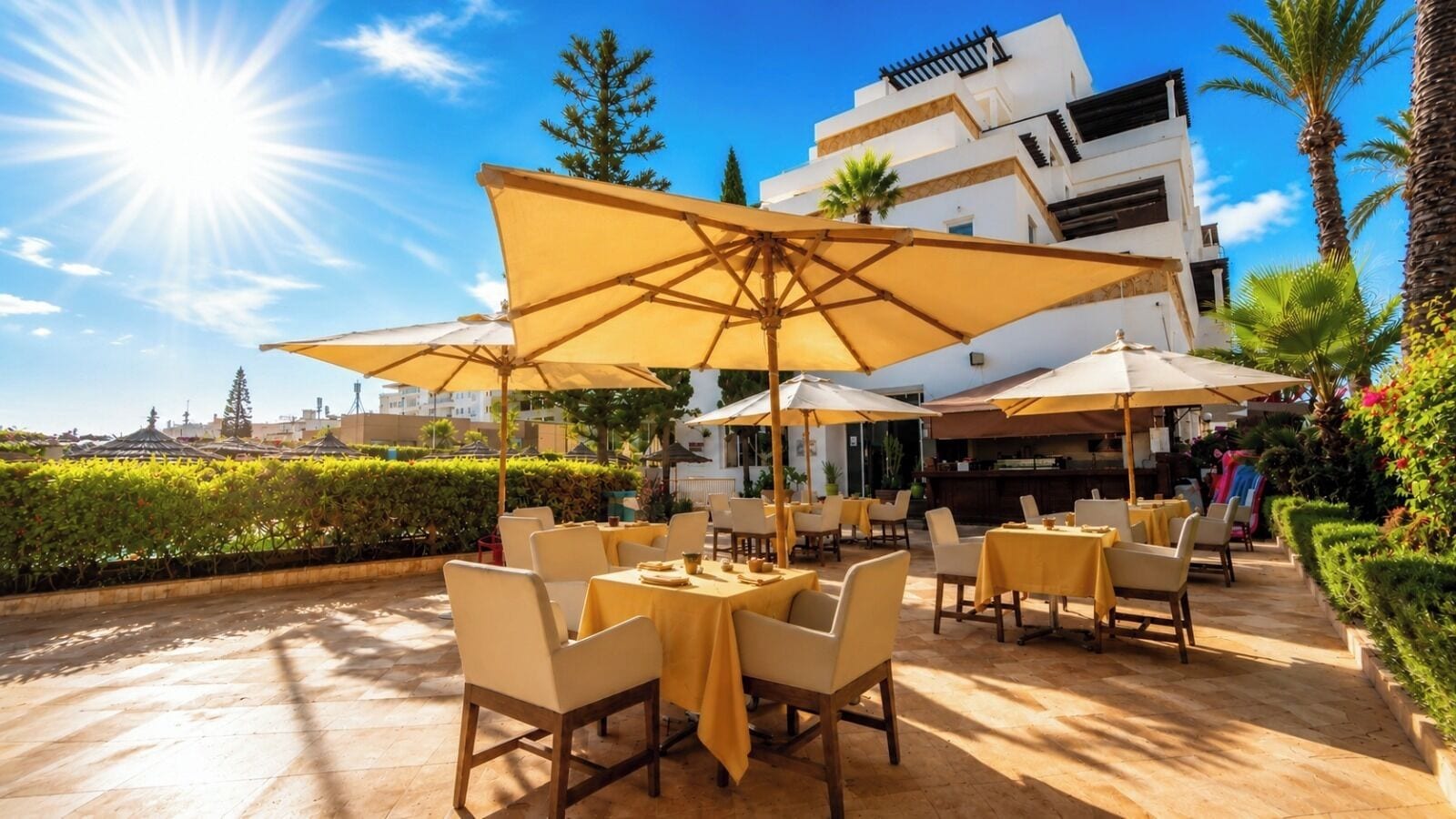 Un patio al aire libre con mesas, sillas y sombrillas, con un edificio al fondo.