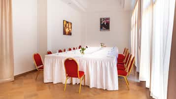Una sala de conferencias con una larga mesa, sillas rojas y manteles blancos.