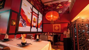 Ein Restaurantinnenraum mit roten Wänden, traditioneller chinesischer Einrichtung und einem für das Essen gedeckten Tisch.