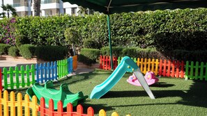 A playground with a slide and a small boat ride, surrounded by a colorful fence.