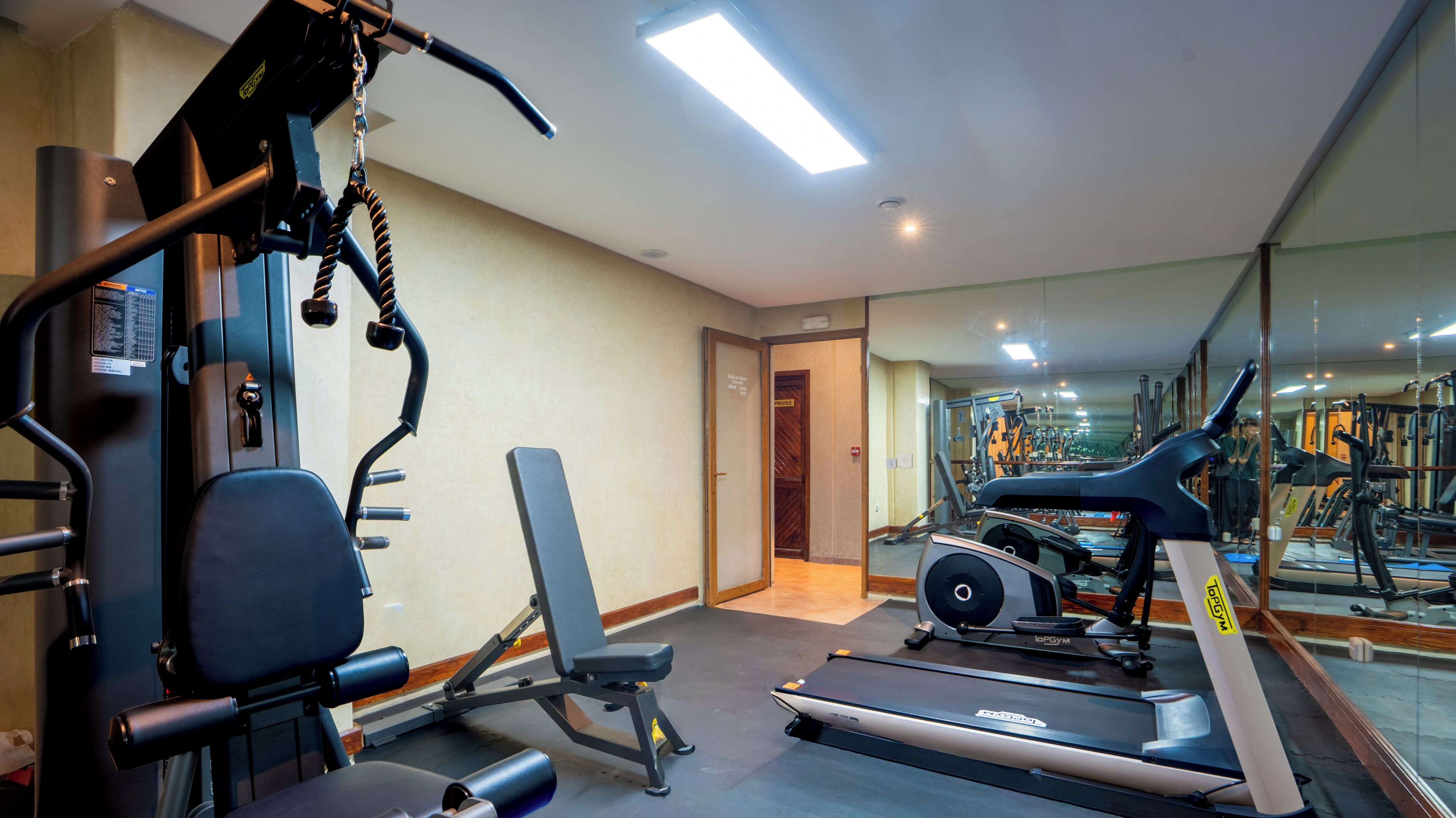Un gimnasio con equipo de ejercicio, cinta de correr y un espejo que refleja el espacio.