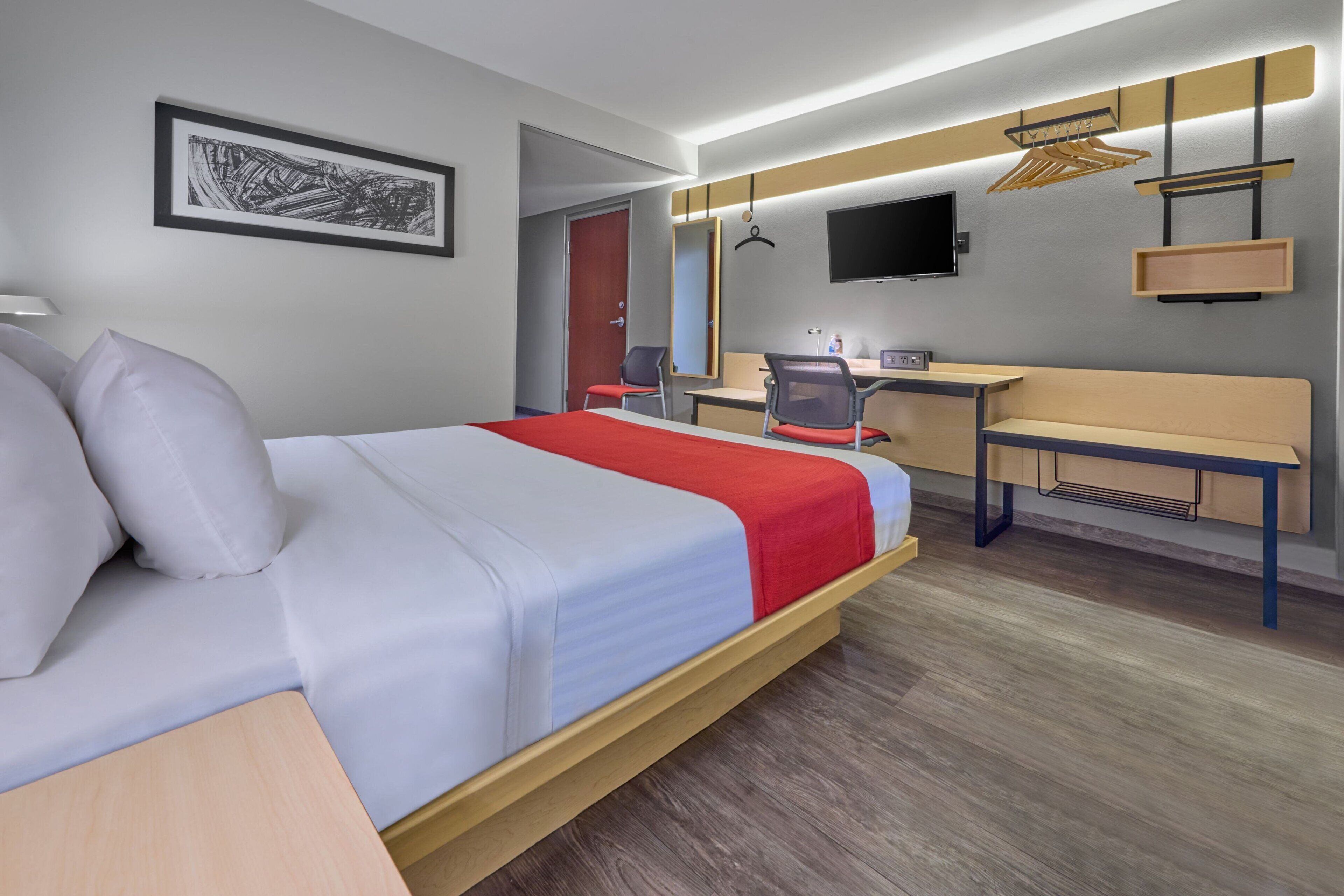 A hotel room with a bed, desk, chair, and a TV mounted on the wall.