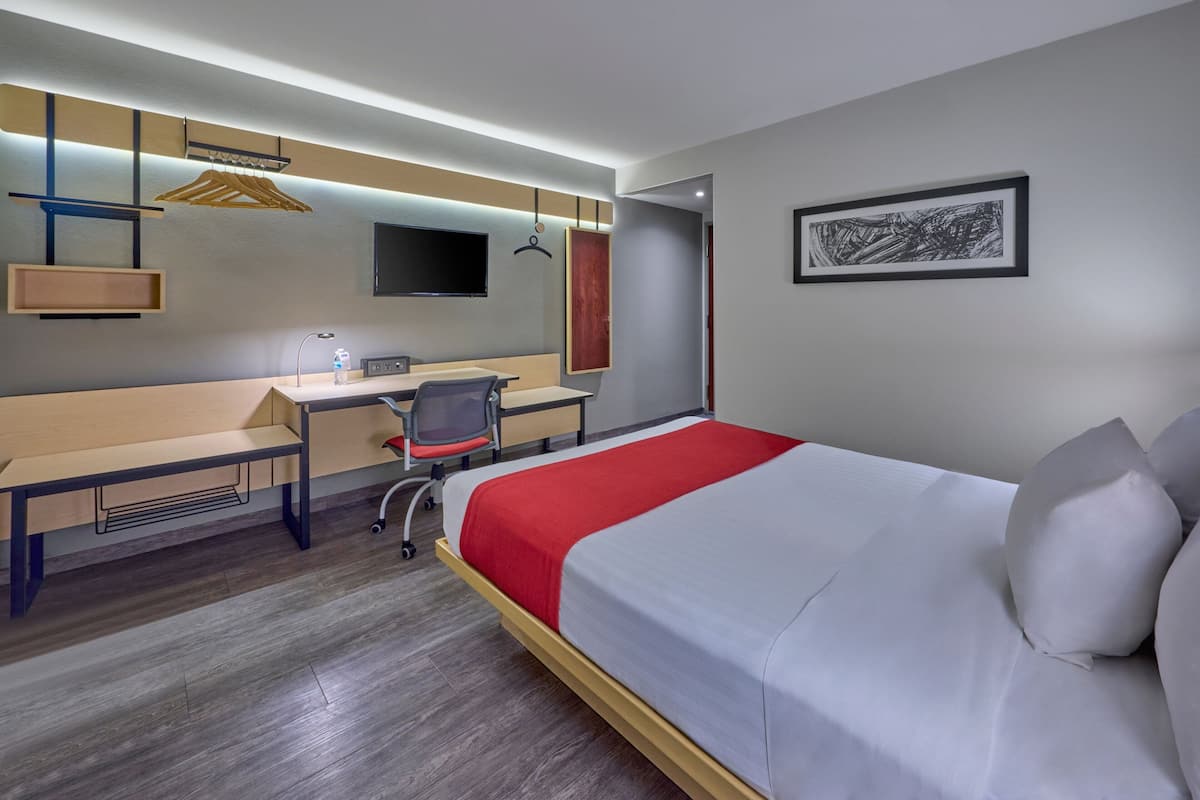 Una habitación de hotel con cama, escritorio, silla y televisor en la pared.