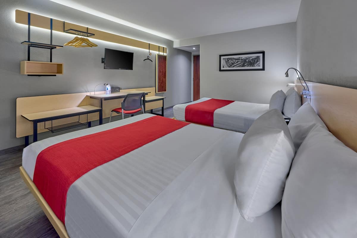 Habitación de hotel con dos camas, un escritorio, una silla, un televisor y una ducha.
