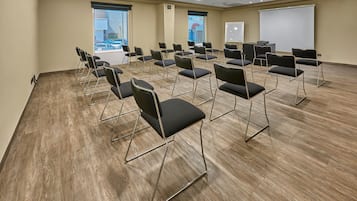 Un salón de conferencias con filas de sillas negras, una pizarra y una pantalla para proyector.
