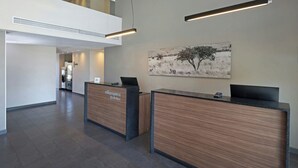 A hotel reception area with two reception desks, a large painting on the wall, and a mezzanine level. - City Express by Marriott Mexicali (Mexicali)