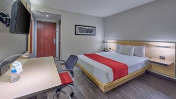 Habitación de hotel con cama, mesitas de noche, escritorio con silla, televisor montado en la pared y una puerta.