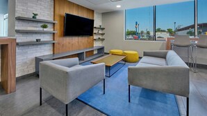 A modern lounge area with grey sofas, a flat-screen TV mounted on a wooden panel, and a large window offering a view of the outside. - City Express by Marriott Mexicali (Mexicali)