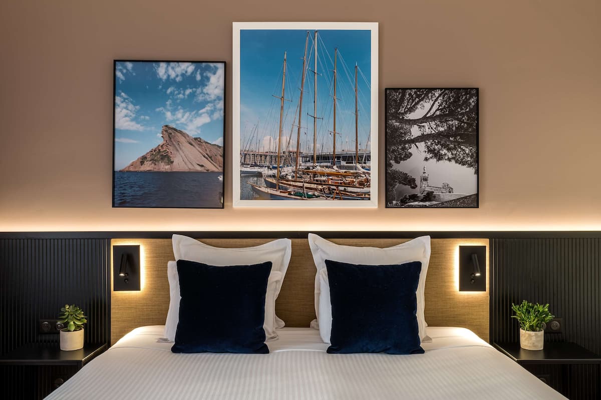 Una camera d'albergo con un letto, due comodini con lampade e tre quadri appesi al muro.