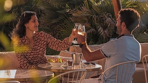 A couple toasting at an outdoor table with a view of a Ferris wheel in the background.