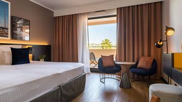 A hotel room with a large bed, a small table, two chairs, and a balcony with curtains.