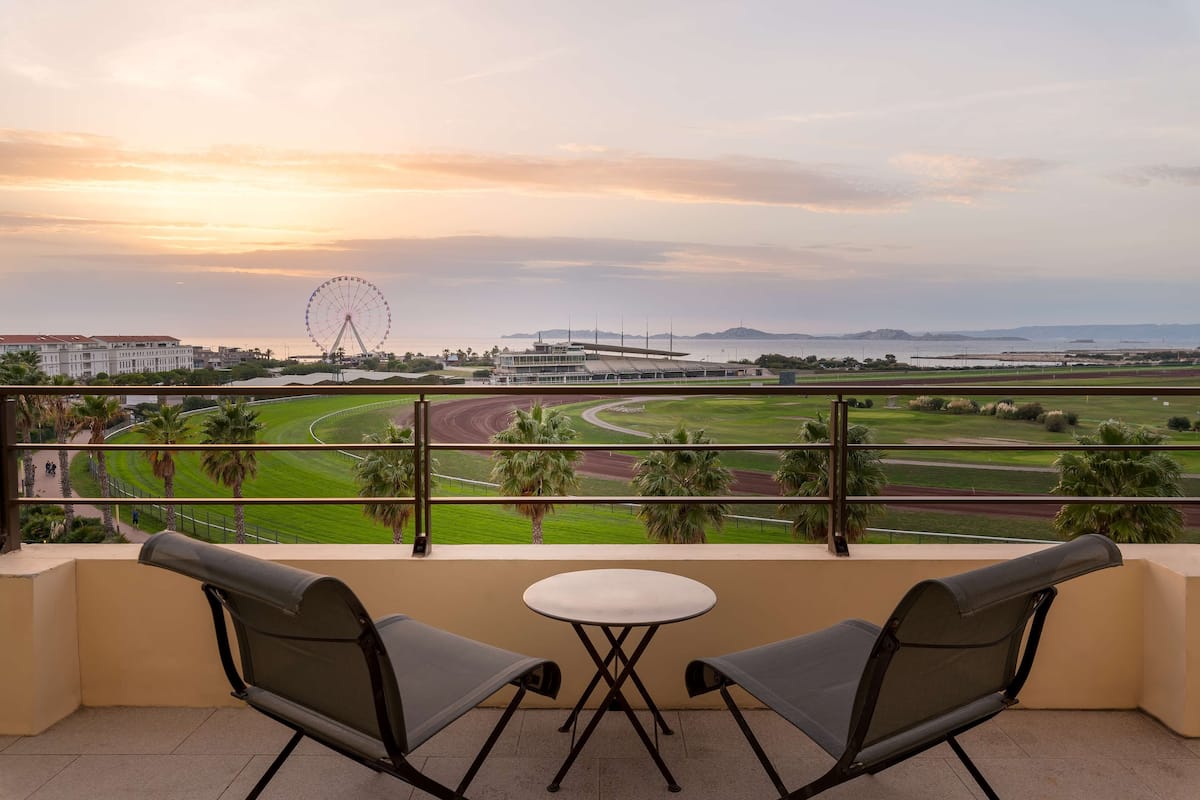 Un balcone con due sedie e un tavolino, affacciato su un campo da golf e una ruota panoramica.