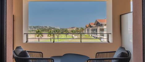 A balcony with two wicker chairs and a small table, overlooking a well-maintained lawn and buildings in the distance.