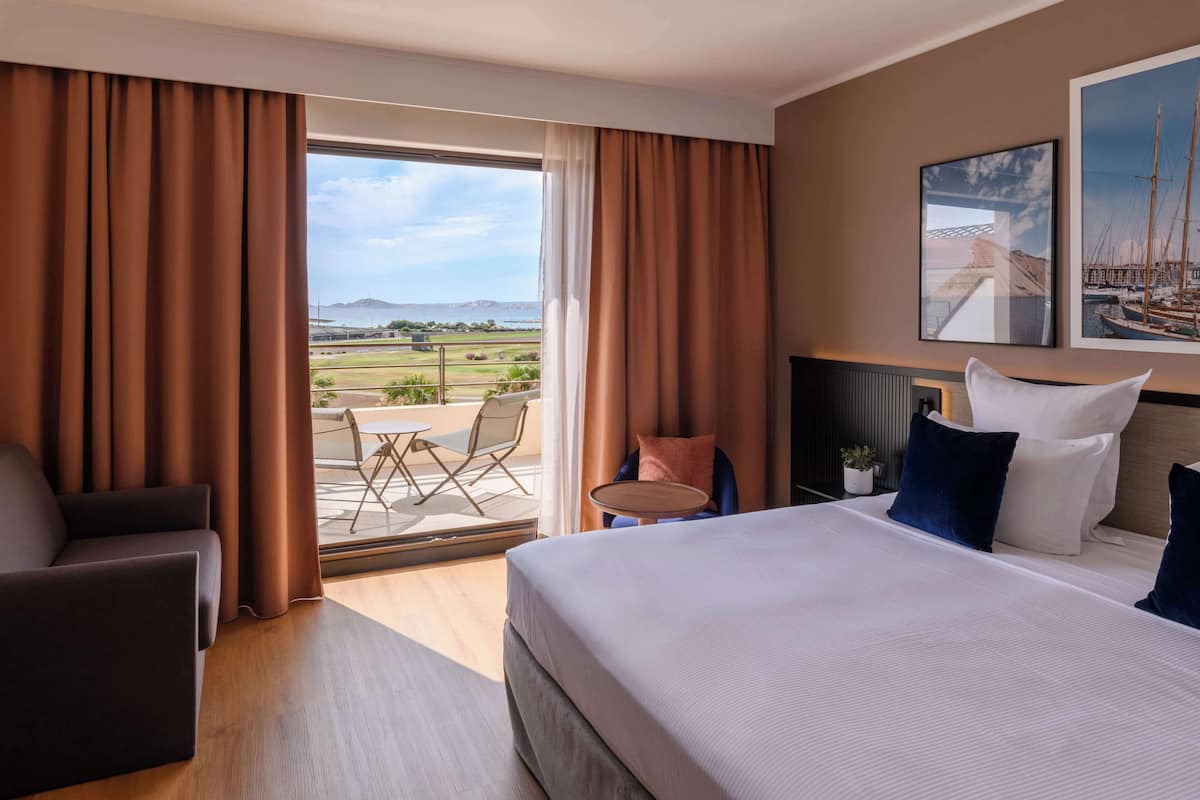 Una camera d'albergo con un letto grande, un divano, un tavolino e vista sull'esterno.
