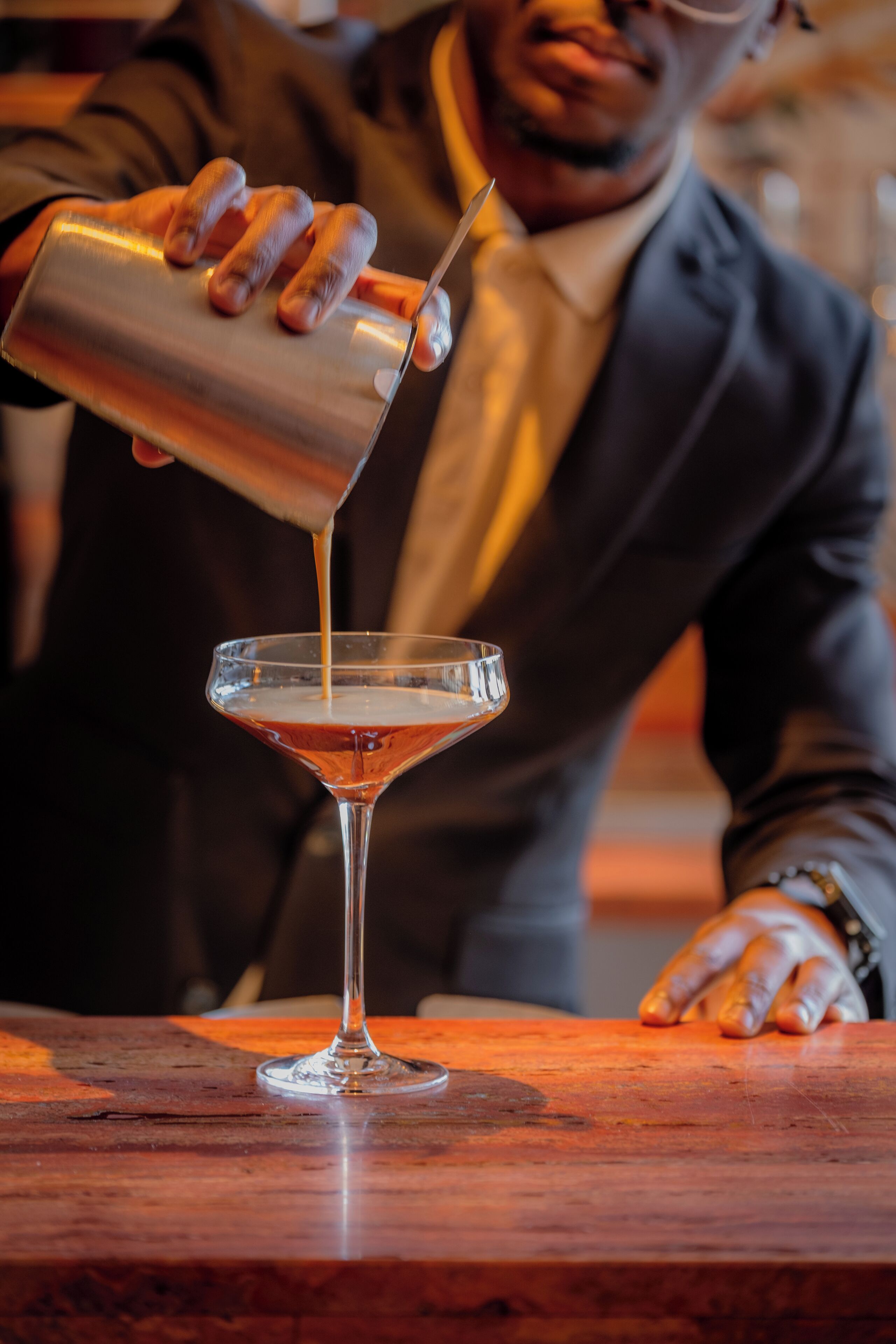 A bartender pouring a drink into a martini glass.