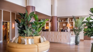 A lobby with a round sofa, large potted plants, a reception desk, and a wooden floor.
