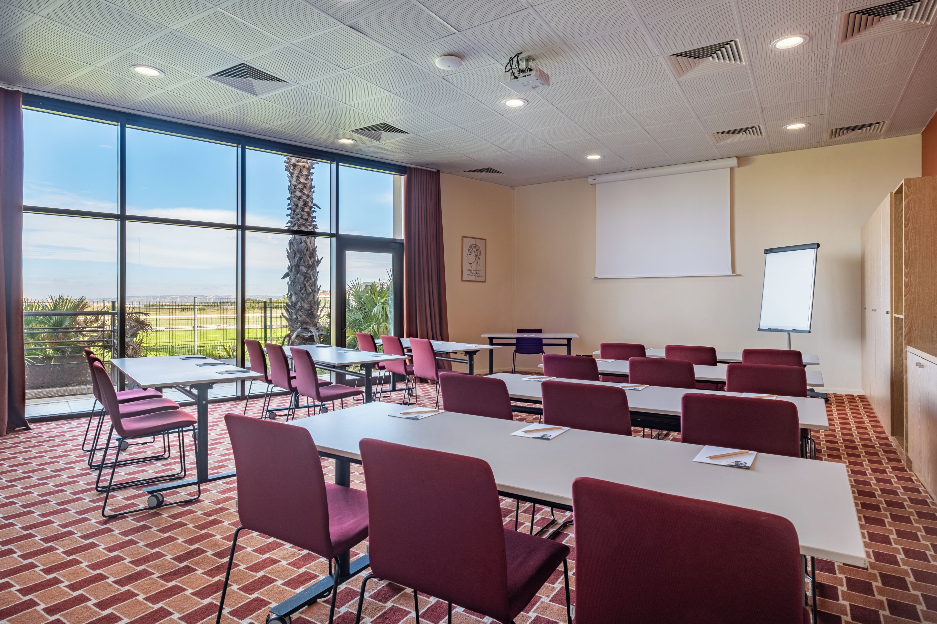 Ein Konferenzraum mit Tischen, Stühlen, einer Projektionsleinwand und einem großen Fenster mit Blick.