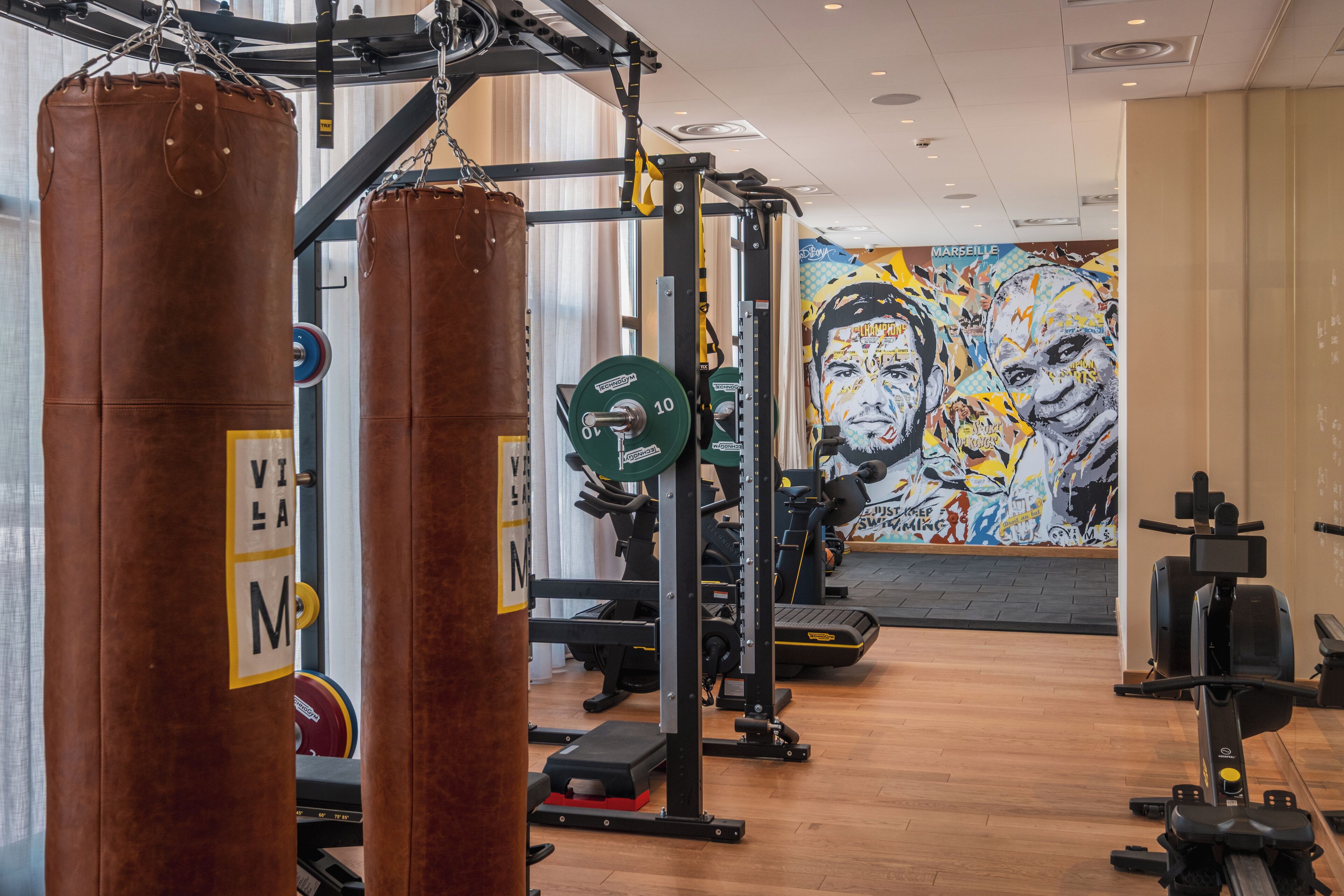 Une salle de sport équipée de matériel de musculation, ornée d’une fresque murale et dotée d’un plancher en bois.