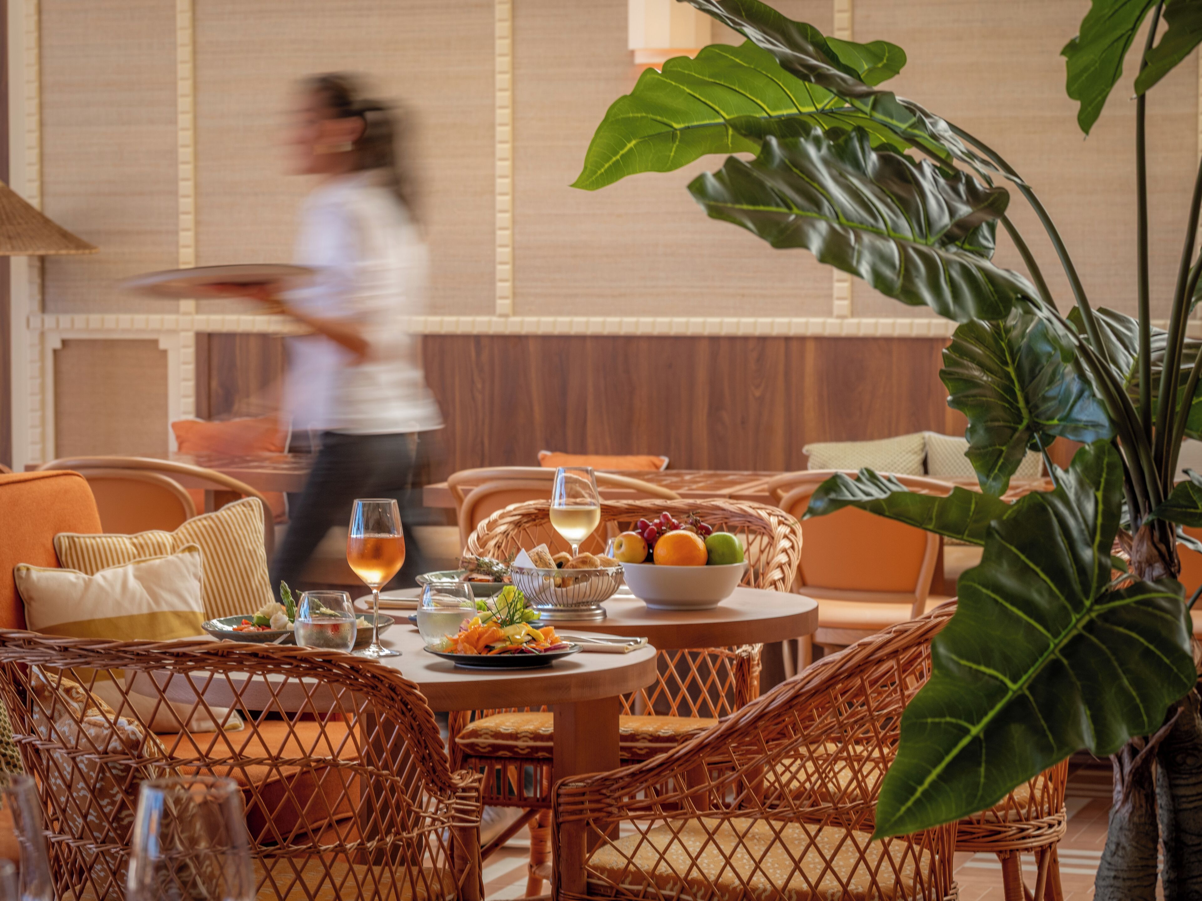 A dining area with wicker furniture, a table set with plates, glasses, and a bowl of fruit.