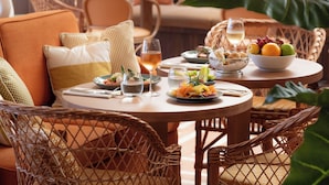 A dining area with wicker furniture, a table set with plates of food, glasses, and a bowl of fruit.