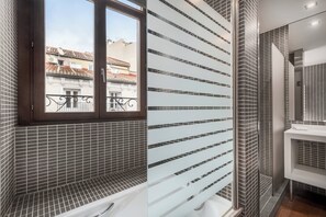 A modern bathroom with a bathtub, a window, and a view of buildings outside. - AC Hotel Recoletos by Marriott (Madrid)