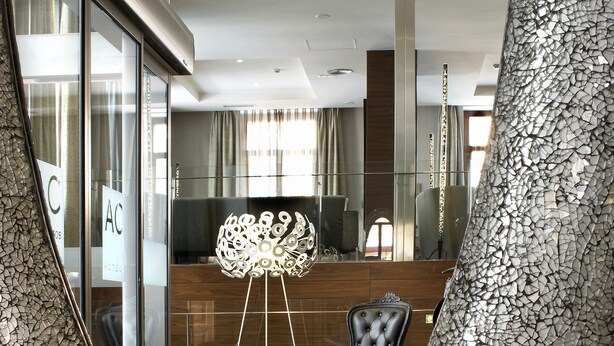 Un vestíbulo moderno con una pared de mosaico única, una lámpara decorativa central y un área de estar con sillón y reposapiés tapizados.
