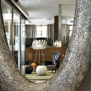 Un vestíbulo moderno con una pared de mosaico única, una lámpara decorativa central y un área de estar con sillón y reposapiés tapizados.