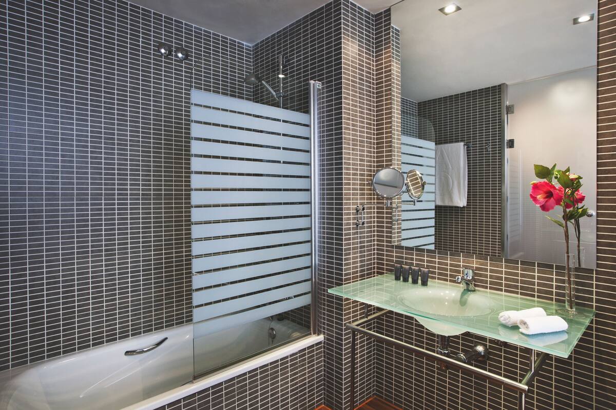 A modern bathroom with a glass sink, a large mirror, and a bathtub.