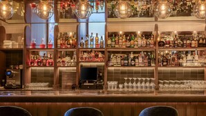 Zona de bar con estantes llenos de botellas de licores, una máquina de café y una pantalla digital.