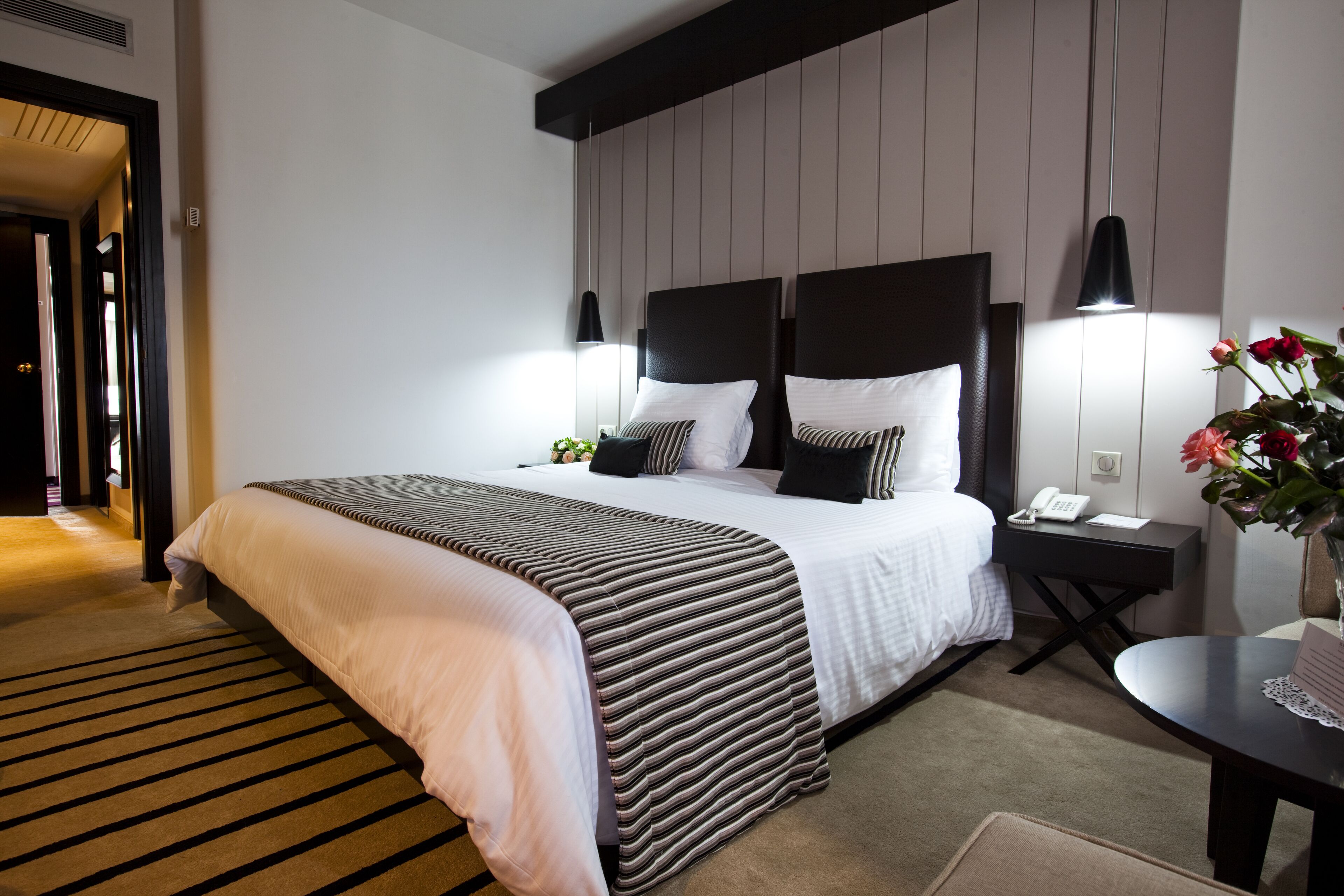 Habitació d'hotel moderna amb un llit gran, petites làmpades de nit, una taula petita amb un ram de flors i un escriptori amb un telèfon.