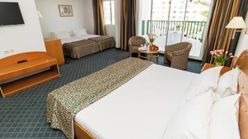 A hotel room with a large bed, a sofa bed, a small table with a fruit bowl, and a chair.