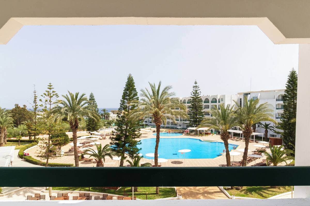 Un complexe hôtelier doté d’une piscine entourée de palmiers et de chaises longues.