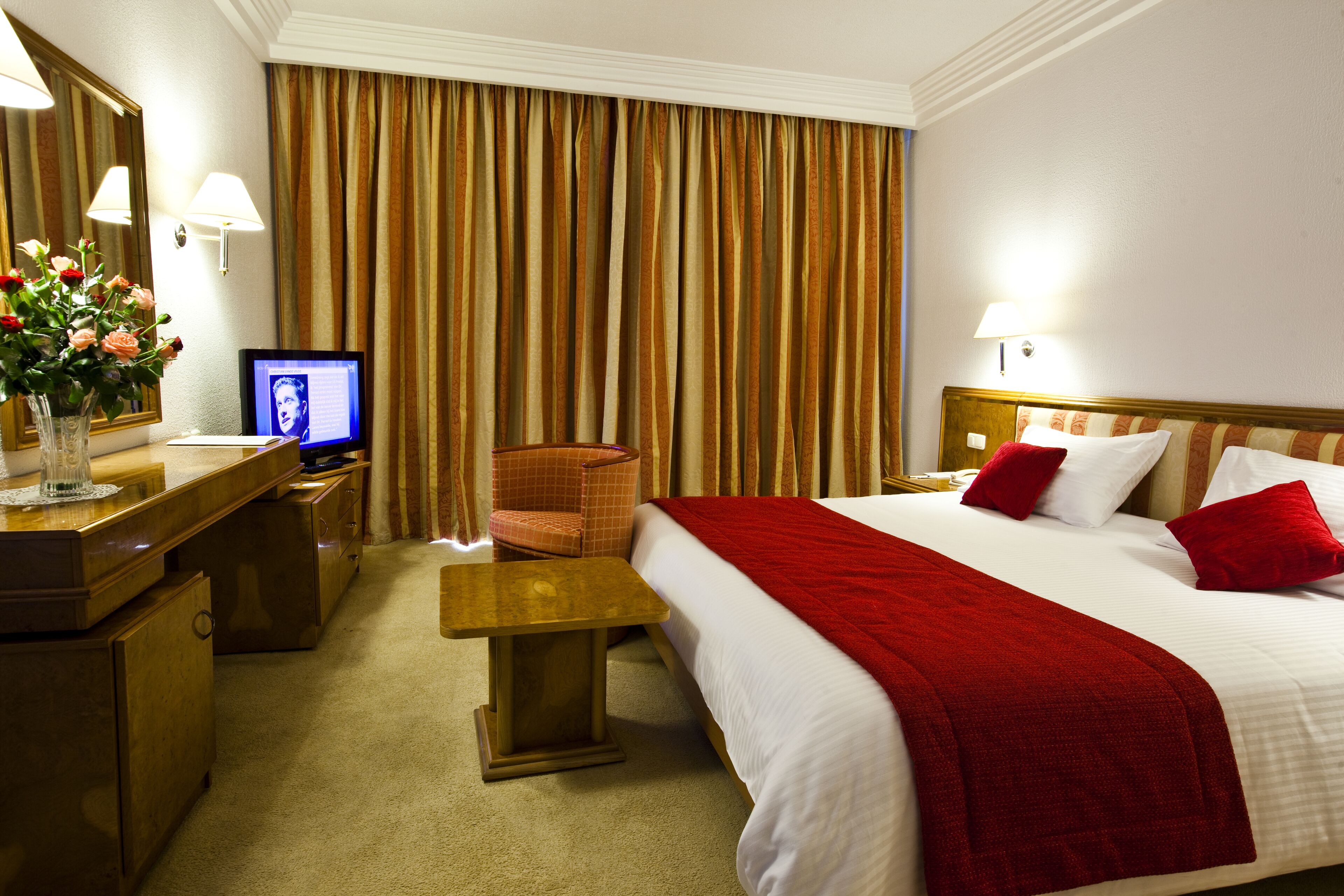 Habitación de hotel con cama, escritorio, silla, televisión y un amplio ventanal con cortinas.