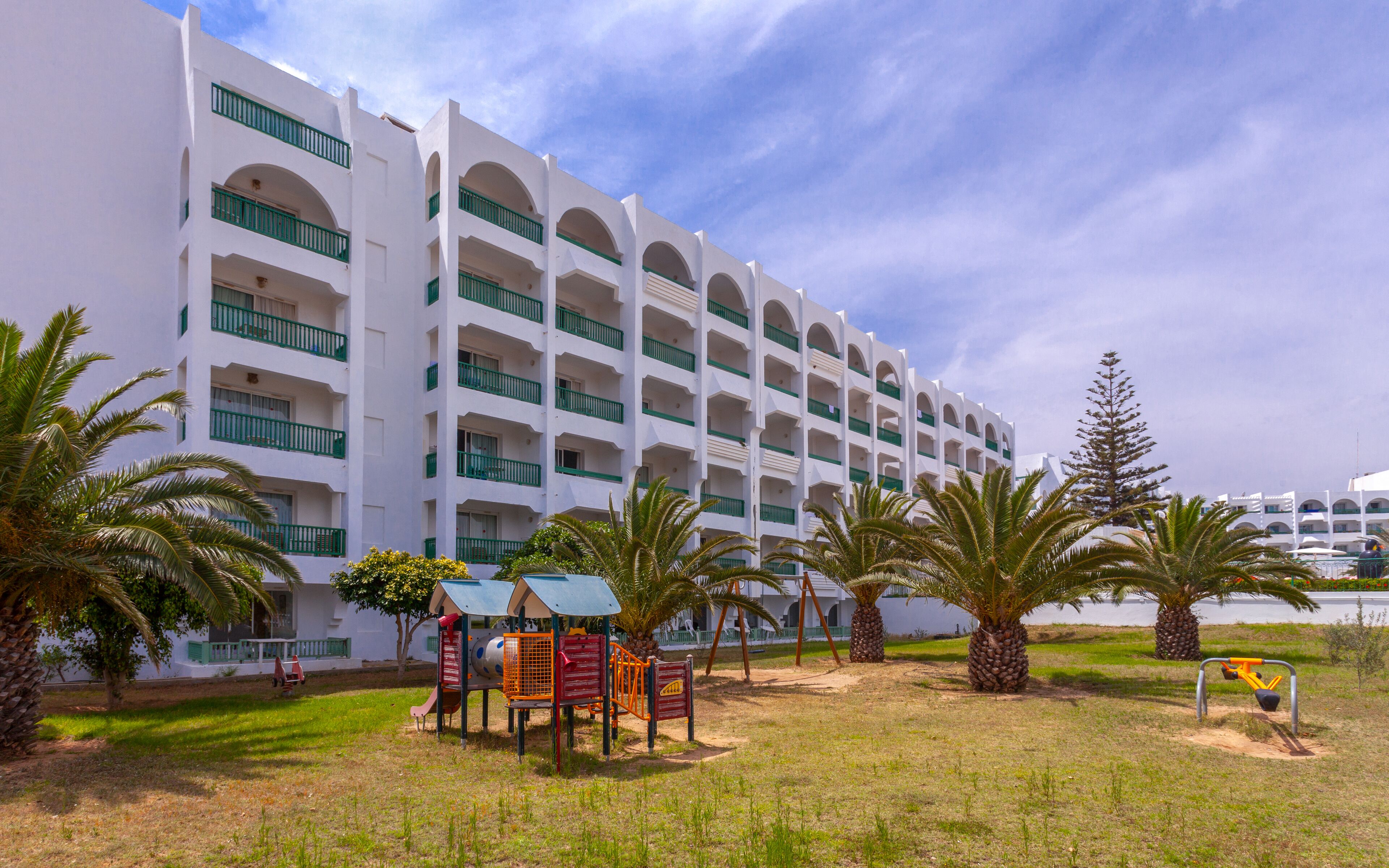 A multi-story hotel with a white facade and green balconies.