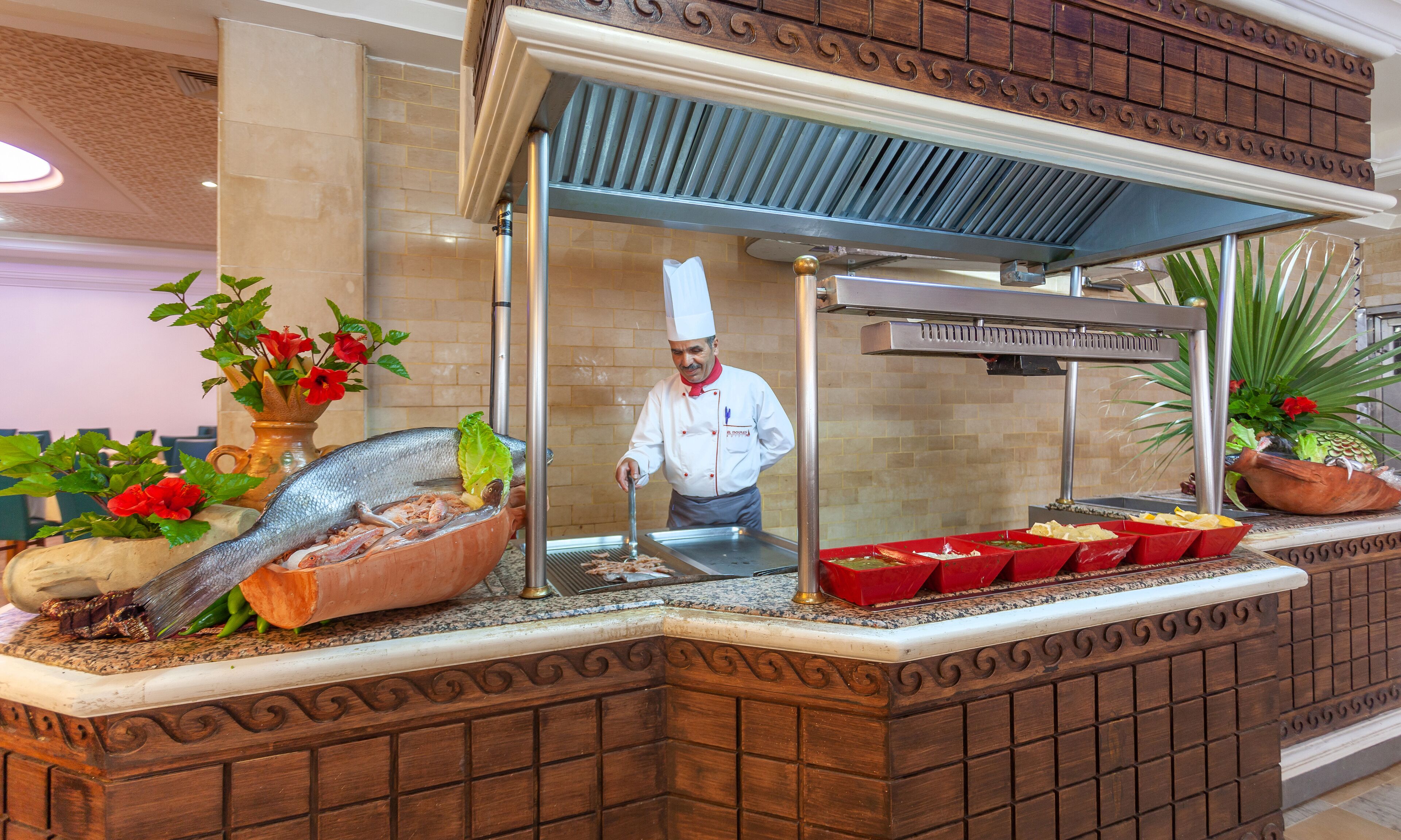A seafood display counter with a chef behind the counter, a decorative fish sculpture, and a variety of seafood dishes.
