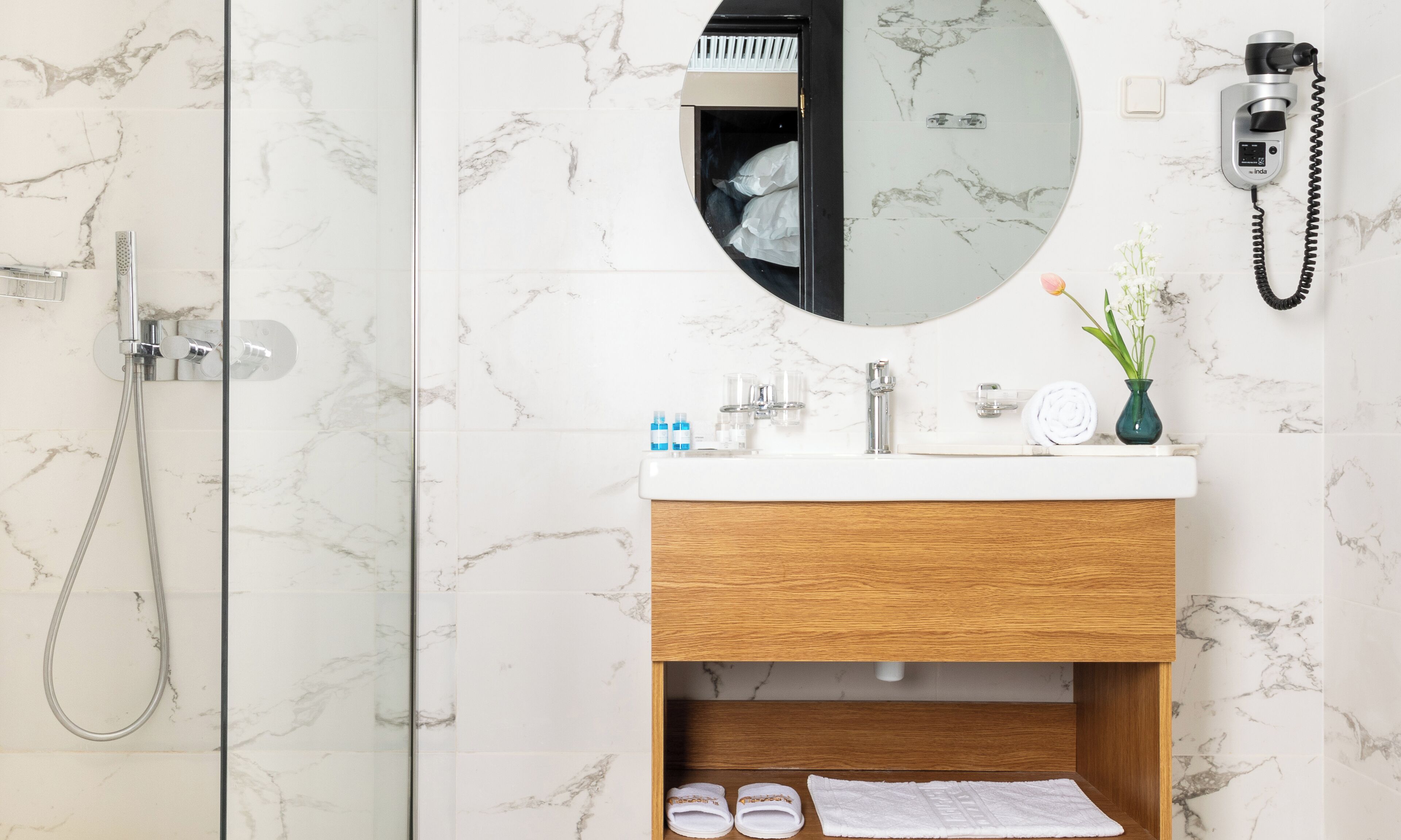 Een moderne badkamer met een douche, een wastafel met spiegel en een aan de muur bevestigde haardroger.