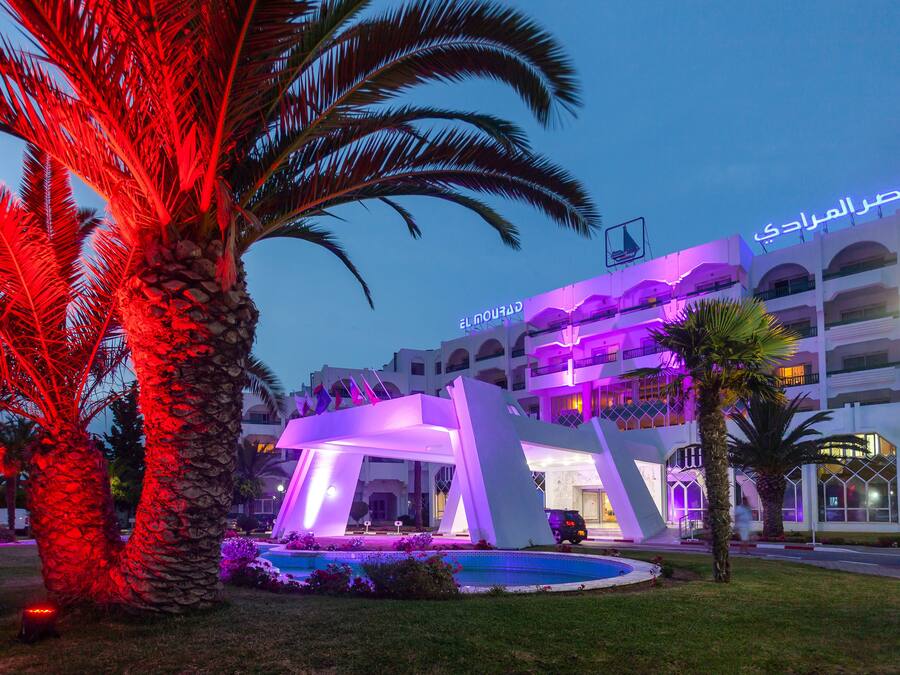 A hotel with a pool, palm trees, and illuminated architecture.