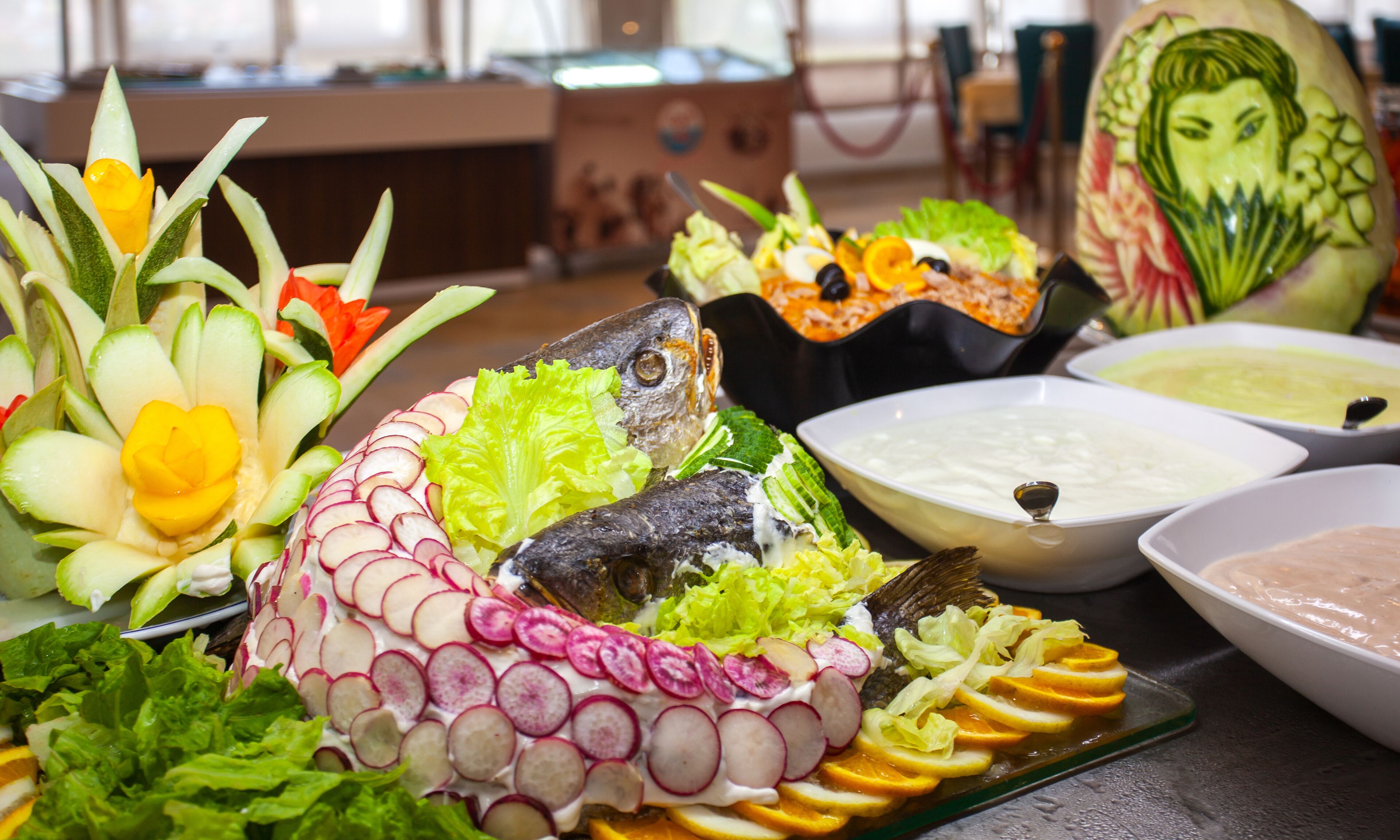 Une table ornée d’un poisson en guise de centre de table, entourée de divers légumes et de bols de soupe.