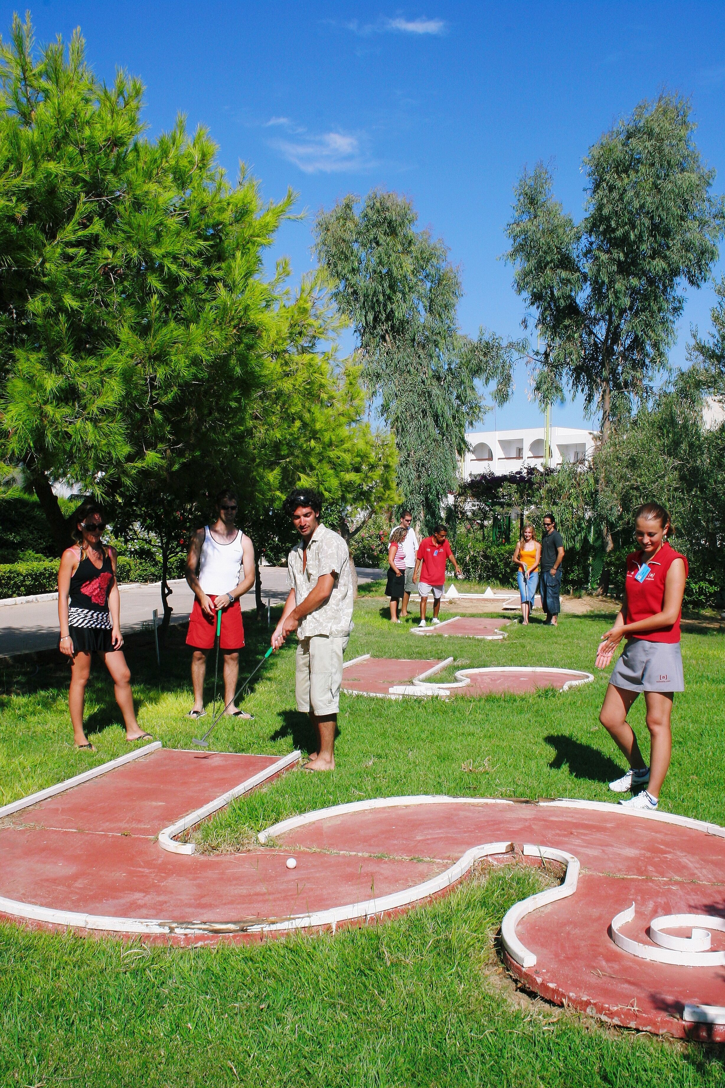 A group of people playing croquet in a park with trees and a building in the background.