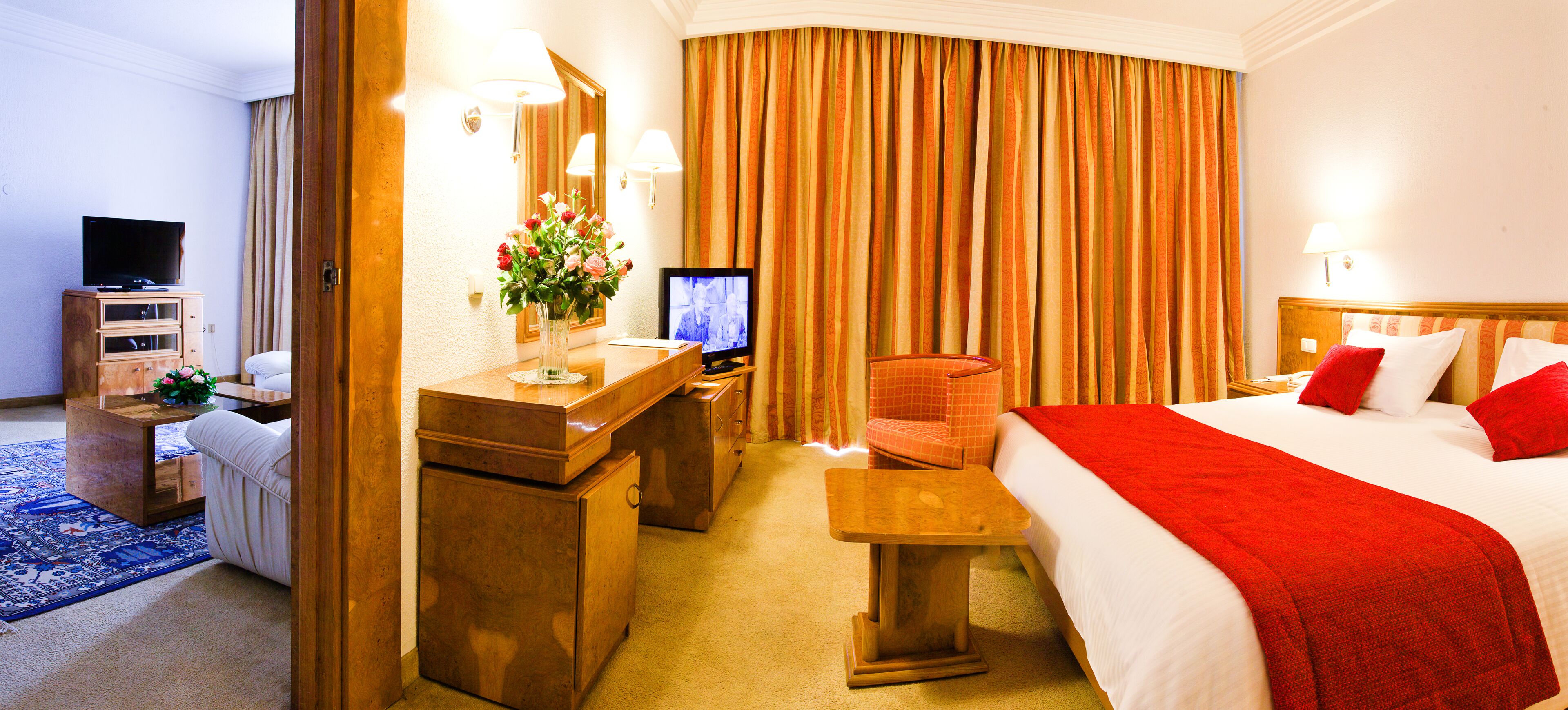 Habitación de hotel con cama, escritorio con televisor, una silla, cómoda y un ventanal con cortinas.