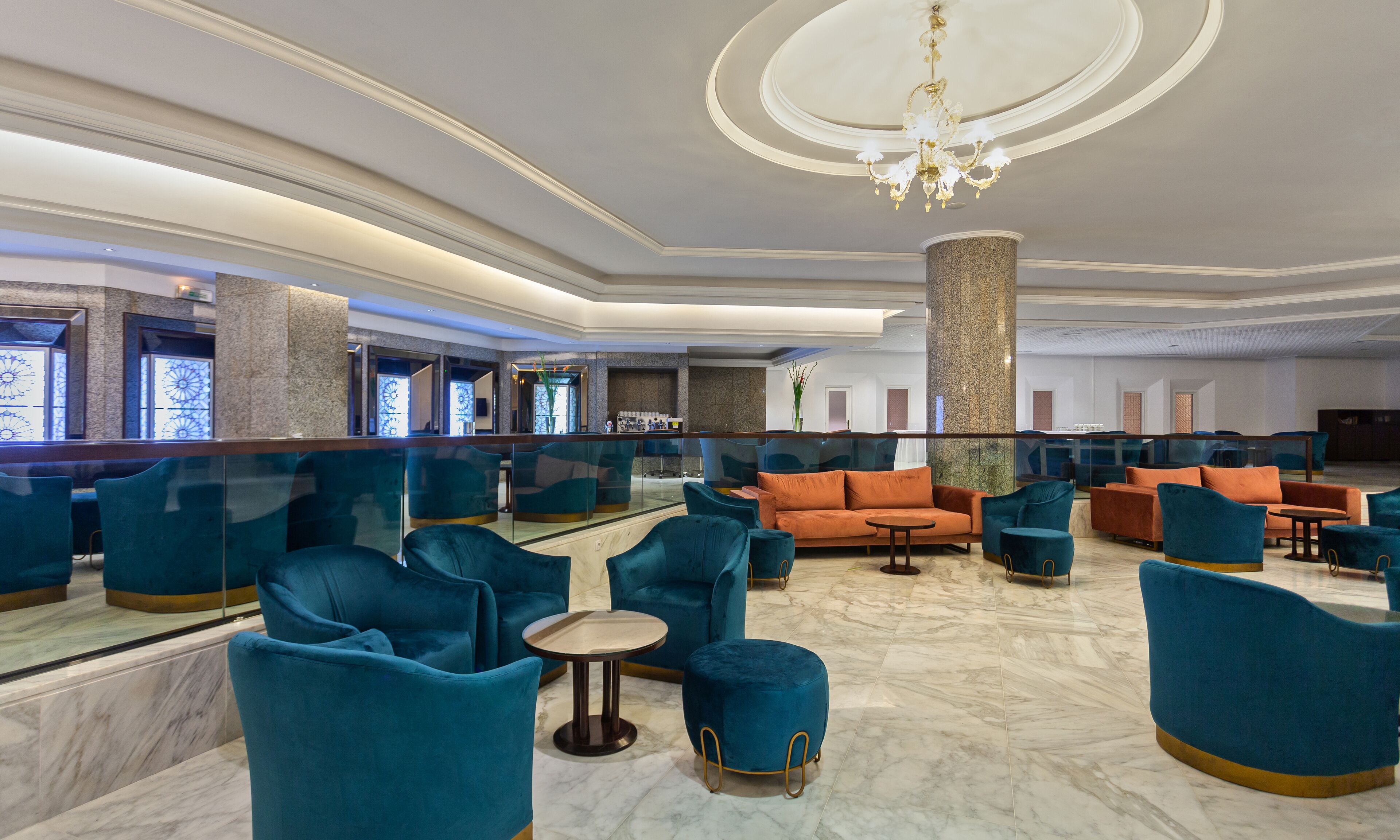 A spacious lobby with teal and orange seating, marble flooring, and a chandelier.